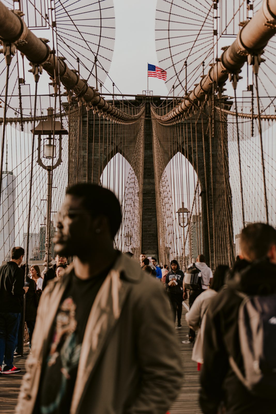 Shawn walking across the Brooklyn Bridge in a crowd, its stone tower and flag behind him