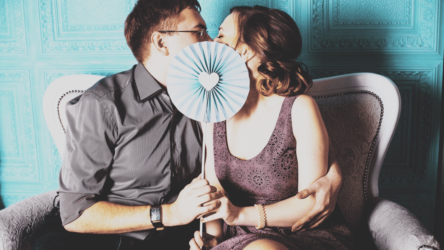 A couple kissing behind a paper fan in an armchair